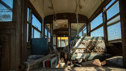 Fototapeta na wymiar Sunlit inside low perspective of old passenger train car with torn and worn seats and debris with blue sky showing through windows