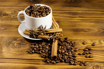 Coffee beans in white cup, cinnamon sticks and star anise on wooden table