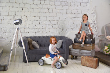 Cute little girls in studio interior. Bags, chairs, white walls, suitcases, toys