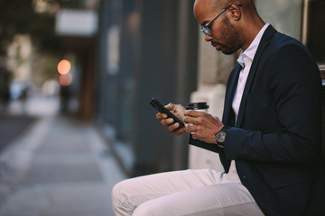 Businessman relaxing outdoors with phone and coffee