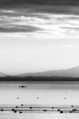 Naklejka premium Beautiful view of Trasimeno lake at sunset with birds on water, a man on a canoe and hills on the background