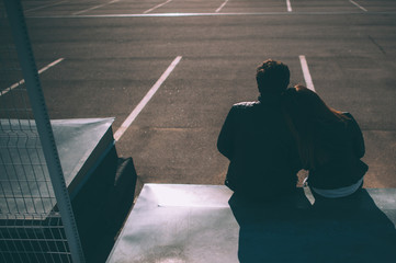 Guy and girl sitting together on the empty parking lot. Romantic couple shoot from behind. Copy space for the text.