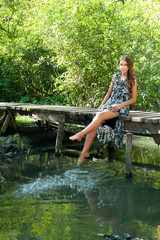 Young beautiful woman sits on wooden bridge and plays with water