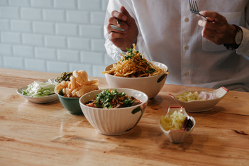 Asian Man eat  Thai Food -Khao Soi with pork snack (Thai Noodle Curry Soup with chicken), Nam Prik Num (Green chili dip) and  Hunglei curry (North curry With tender pork) over the wooden table