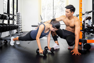 Fototapeta na wymiar Personal trainer coaching female bodybuilder lifting dumbbell at the gym