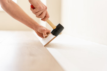 Strikes with a soft hammer on the part with a lock, for fixing. Installing laminate flooring fitting the next piece - focus on hand. Man laying laminate flooring