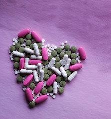 White, pink and green pills laid out in the shape of a heart on a pink background. multi-colored drugs. concept - heart disease, heart disorders and drugs, cardiology.
