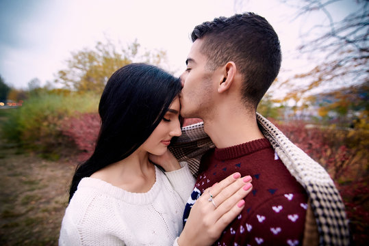 beautiful girl in a white sweater and long black hair stands wrapped in a blanket in an embrace with a guy who kisses her on the forehead