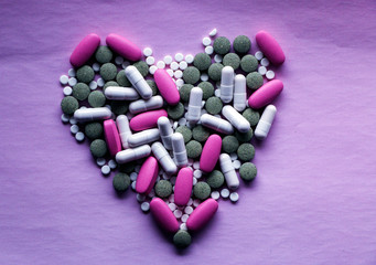 White, pink and green pills laid out in the shape of a heart on a pink background. multi-colored...