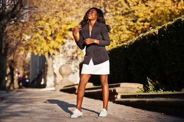 Success stylish african american woman in jacket and skirt posed on sunny autumn day at street.