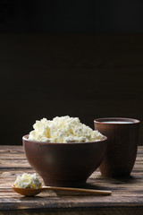 Fresh cottage cheese in  clay bowl with wooden spoon with a glass of milk on rustic wooden background
