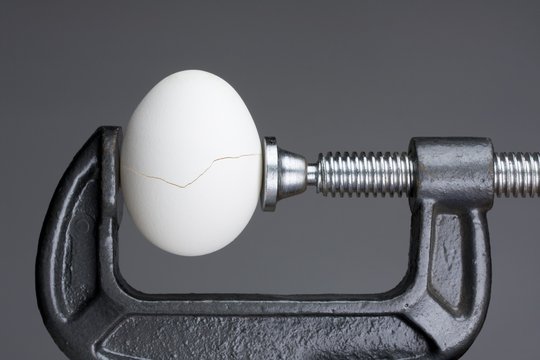 Under pressure.An egg cracking under pressure applied by squeezing clamps form the sides.