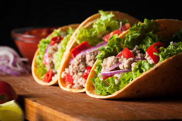 Photo of Mexican tacos with ground beef, onion, tomatoes, chili, red sauce, lettuce and lime on wooden background. Spicy and fast food concept.