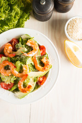 Fresh Caesar shrimp salad with delicious prawns, ruccola, spinach, cabbage, arugula, egg, parmesan and cherry tomato on wooden background. Oil, salt and pepper. Healthy and diet food concept.