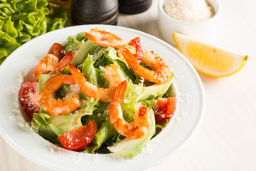 Fresh Caesar shrimp salad with delicious prawns, ruccola, spinach, cabbage, arugula, egg, parmesan and cherry tomato on wooden background. Oil, salt and pepper. Healthy and diet food concept.