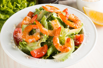 Fresh Caesar shrimp salad with delicious prawns, ruccola, spinach, cabbage, arugula, egg, parmesan and cherry tomato on wooden background. Oil, salt and pepper. Healthy and diet food concept.