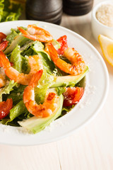 Fresh Caesar shrimp salad with delicious prawns, ruccola, spinach, cabbage, arugula, egg, parmesan and cherry tomato on wooden background. Oil, salt and pepper. Healthy and diet food concept.