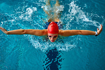 Female athlete swims with a butterfly style. Splashes of water scatter in different directions.
