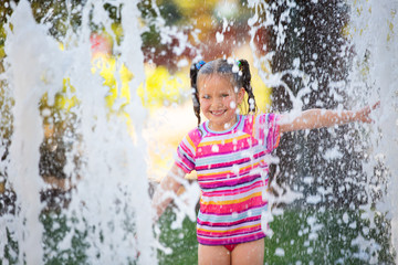 Small girl with 2 pony tails in pink striped rush guard swim suit having fun in a city fountain on...