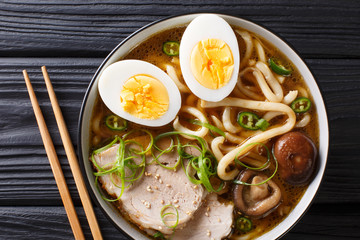 Traditional Japanese udon noodle soup with pork, boiled eggs, mushrooms and green onions closeup in...