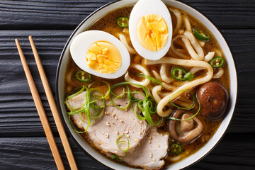 Spicy udon noodle soup, pork, boiled eggs, shiitake and onions close-up in a bowl. Horizontal top...