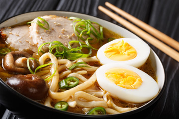 Spicy udon noodle soup, pork, boiled eggs, shiitake and onions close-up in a bowl. horizontal