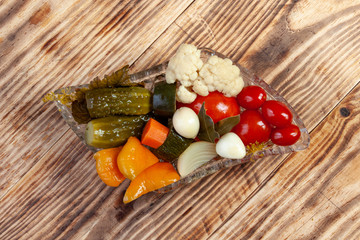 Different types of vegetables in vase. Pickled cucumbers, tomato cherry, greens, сauliflower, zucchini, carrots and garlic with onion and sweet pepper served on crystal vase.