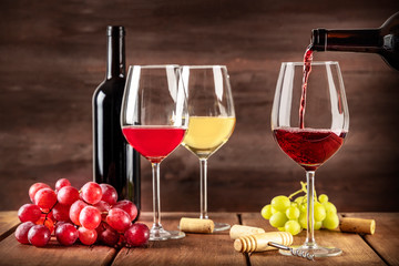 Wine Tasting. Red wine poured into a glass from a bottle with copy space and other glasses and grapes in the blurred dark rustic background