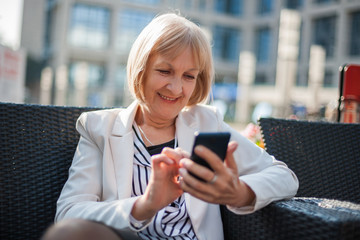 Senior businesswoman is sitting in cafe and searching for job on internet.
