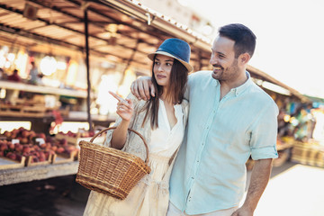 Young couple buying fruits and vegetables in a market on a sunny morning.