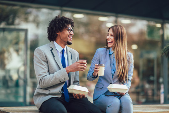 Smiling businessmen with paper cups sitting  in front of the office building - lunch break