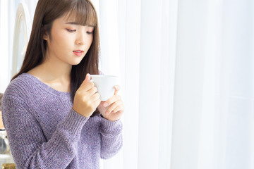 Asian woman holding a cup of coffee in her hands on the light background from window.She dress sweater violet colour.Morning coffee  time.