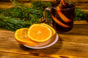 Cup of mulled wine with cinnamon, sliced orange and fir tree branches on wooden table