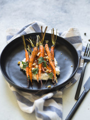 Baked young orange carrots with soft cheese, walnuts and cilantro on plate.