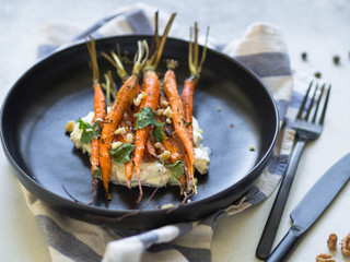 Baked young orange carrots with soft cheese, walnuts and cilantro on plate.