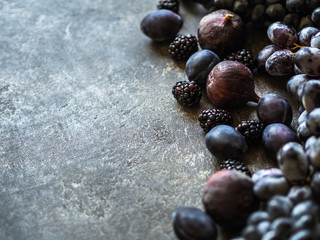 Purple fruits and berries border. Blackberries, grapes, plums and figs on dark background. Tasty and ripe fruits and berries. Copy space