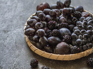 Purple fruits and berries. Blackberries, grapes, plums and figs in a wooden tray on dark background. Tasty and ripe fruits and berries. Copy space