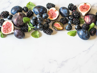 Naklejka na ściany i meble Purple fruits, berries and mint leaves border. Blackberries, grapes, plums and figs on white marble background. Tasty and ripe fruits and berries. Copy space Top view