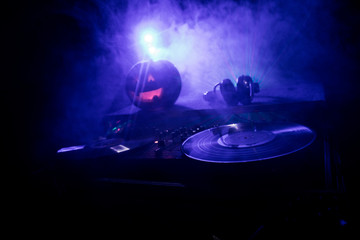 Halloween pumpkin on a dj table with headphones on dark background with copy space. Happy Halloween festival decorations and music concept