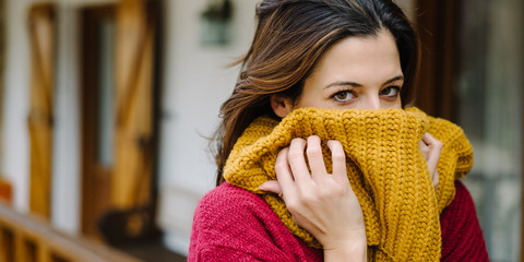 Playful young woman covering her face with  yellow scarf outside her home in autumn cold season.