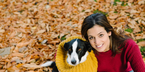Happy woman with her dog enjoying autumn season together. Funny cute pet wearing warm scarf.