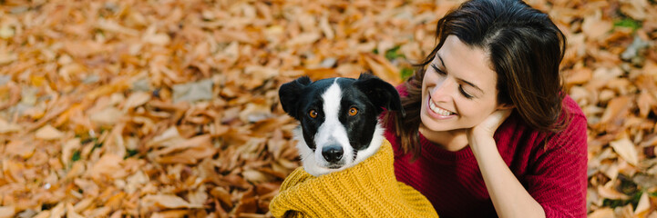 Happy woman with her dog enjoying autumn season together. Funny cute pet wearing warm scarf.