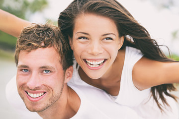 Happy couple having fun piggybacking laughing on summer honeymoon holidays vacation on beach. Beautiful interracial multi-ethnic dating people on wedding, Caucasian man and Asian woman.