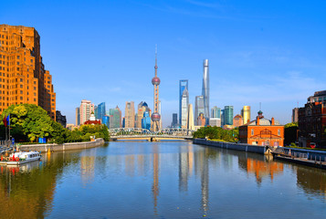 historical Waibaidu bridge with water reflections and colorful blue sky in front of the futuristic modern skyline of Pudong Shanghai, China