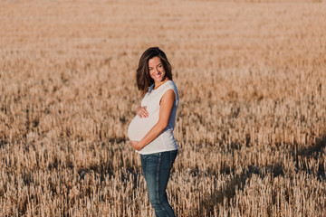 portrait outdoors of a young beautiful pregnant woman touching her belly while expecting a baby. Outdoors lifestyle. Yellow background