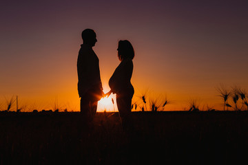Fototapeta na wymiar silhouette outdoors of a young young pregnant couple in a yellow field. Outdoors family lifestyle.