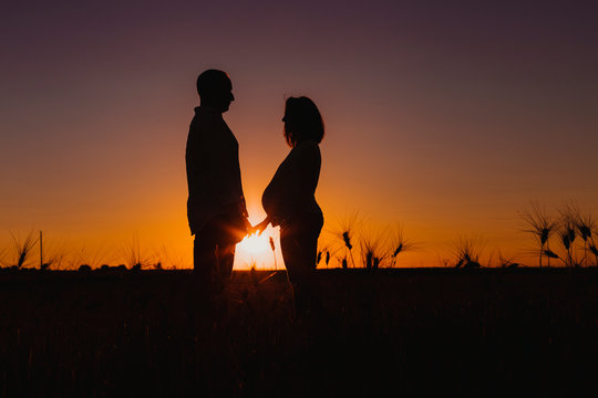 silhouette outdoors of a young young pregnant couple in a yellow field. Outdoors family lifestyle.