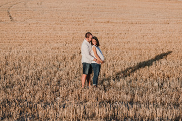 Naklejka na ściany i meble portrait outdoors of a young young pregnant couple in a yellow field. Outdoors family lifestyle.
