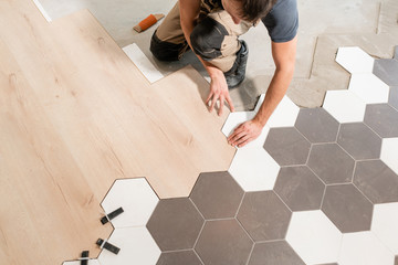 Male worker installing new wooden laminate flooring. The combination of wood panels of laminate and ceramic tiles in the form of honeycomb. Kitchen renovation.