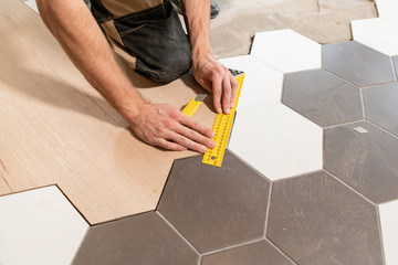 Male worker makes measurements and installing new wooden laminate flooring. The combination of wood...